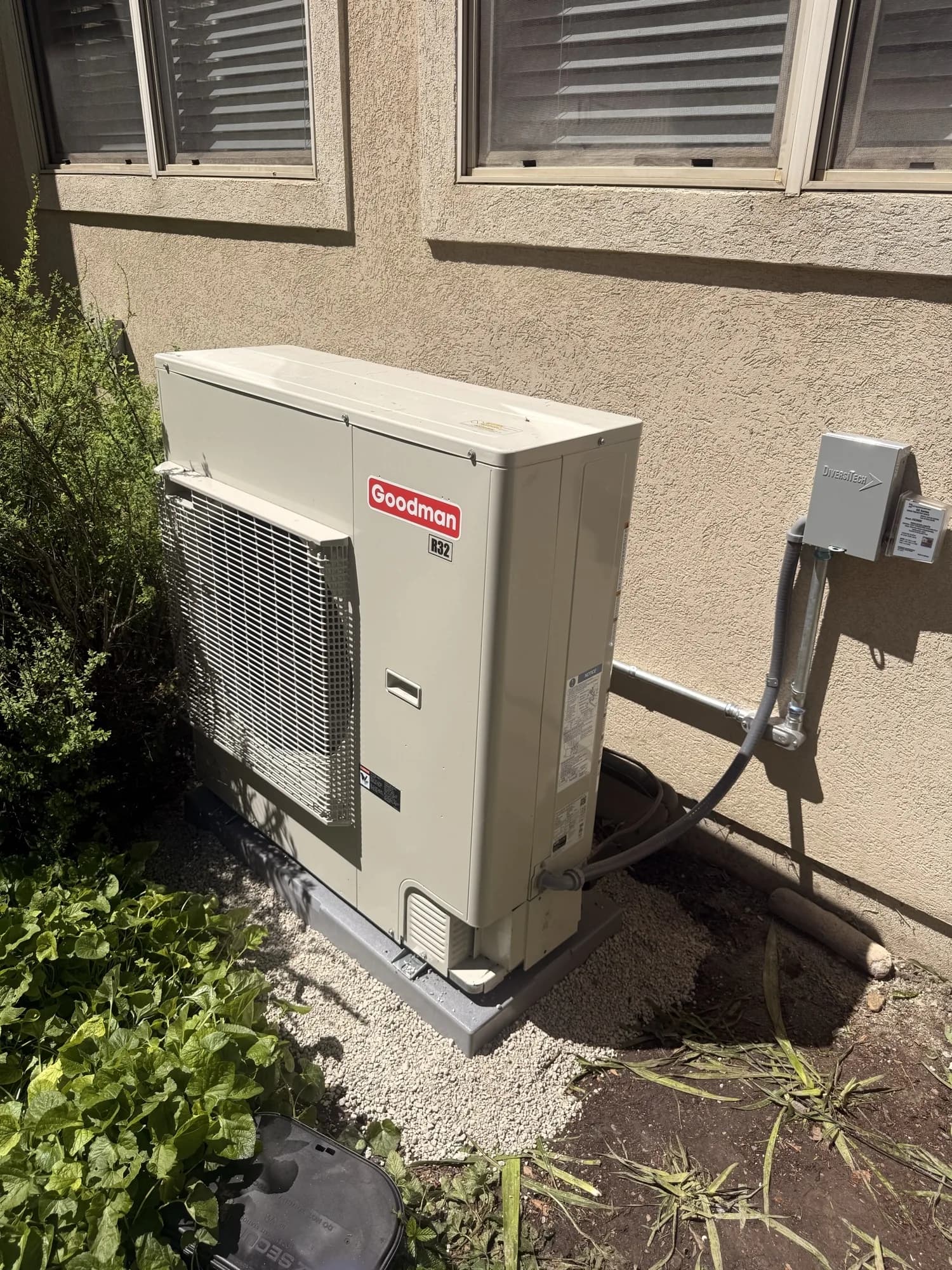 Side-discharge heat pump installed on a gravel pad against a stucco wall