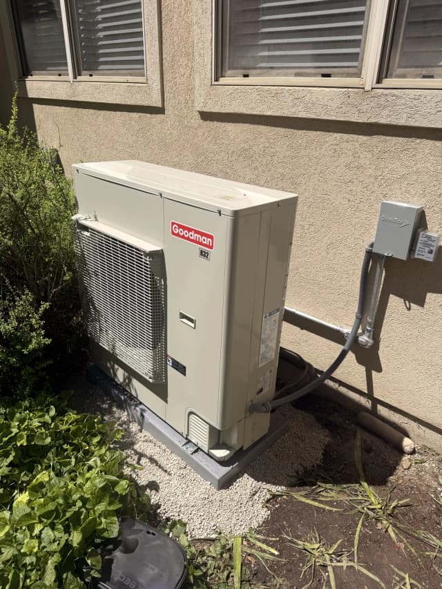 Side-discharge heat pump installed on a gravel pad against a stucco wall